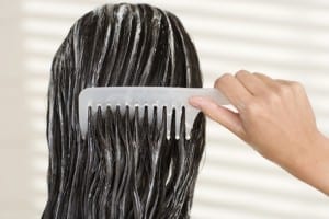 A woman combing her hair that is full of wet shampoo.