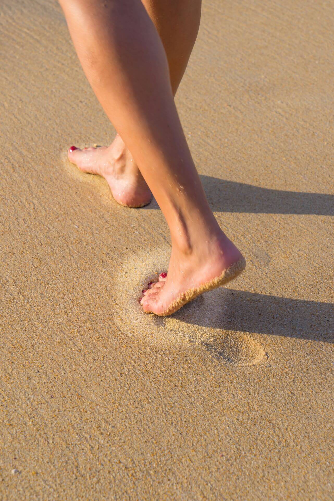 A woman walking on wet sand, showing the dry appearance of the sand directly under the foot.